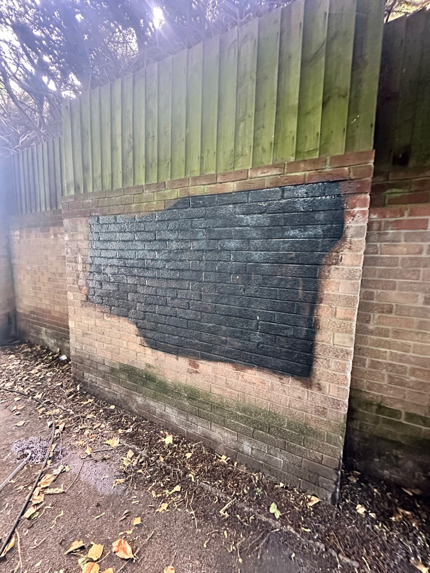 Before graffiti cleaning: tagged brick wall section with dense black paint across the centre
